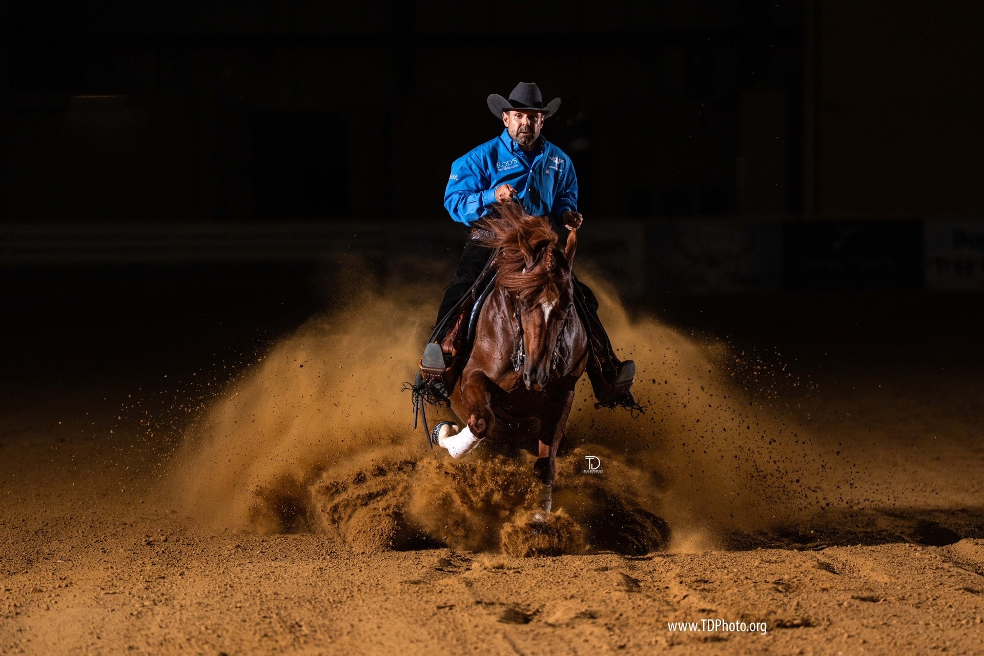 Robin Schoeller performing a dramatic sliding stop on a dark bay horse in an indoor arena